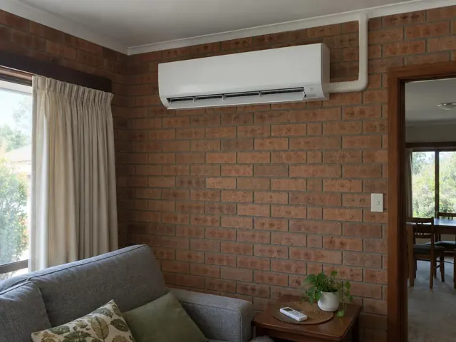 Wall-mounted split system on a brick feature wall in a living room with curtains and sofa in Valley View