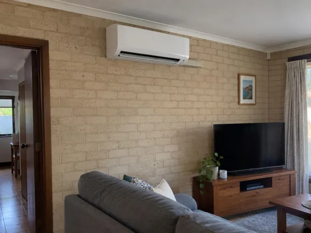 Wall-mounted split system on a brick living room wall above a TV in Hope Valley